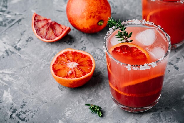 Sangría de naranja sanguina con hielo y tomillo sobre fondo oscuro