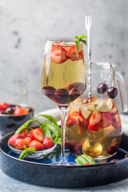 Sangría de vino blanco o ponche con frutos rojos y hielo en copa y pincher. Sangría de frutas refrescante casera.