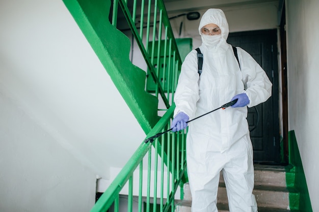 Sanitärfachmann im Schutzanzug desinfiziert einen Wohnblock im Treppenhaus. Maßnahmen zur Vorbeugung von Coronaviren in Wohngebieten.