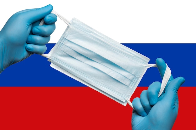 Sanitäter mit Atemschutzmaske in blauen Handschuhen auf Hintergrundfahne der Russischen Föderation...