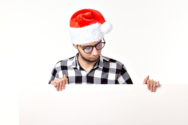 Foto santa bärtiger mann, brutaler hipster mit schnurrbart auf überraschtem gesicht in weihnachtlichem rotem hut für neujahrsferien mit weißem papierblatt isoliert auf weißem hintergrund, kopierraum.