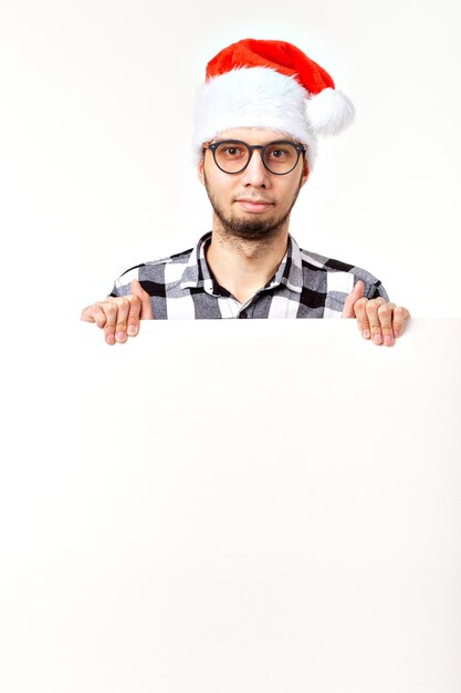 Foto santa barbudo homem, hipster brutal com bigode no rosto surpreso no chapéu vermelho de natal para o feriado de ano novo com folha de papel branco isolada no fundo branco, copie o espaço.