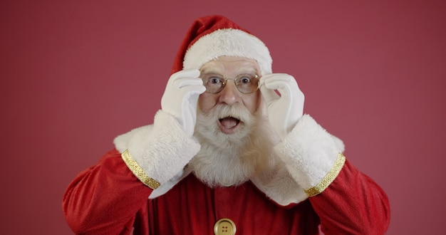 Santa Claus en anteojos está mirando a la cámara y sonriendo, sobre fondo rojo.