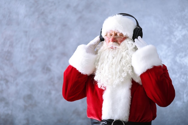 Santa Claus con auriculares escuchando música sobre fondo de pared gris