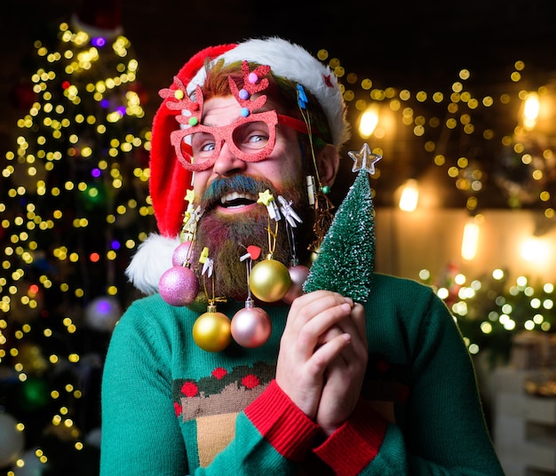 Santa claus barbudo con gafas de fiesta sostiene un pequeño árbol de navidad estilo barba de navidad feliz santa