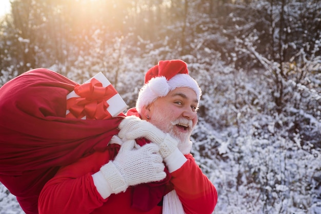 Santa claus caminando hacia el bosque de invierno con una bolsa de regalos paisaje nevado feliz año nuevo