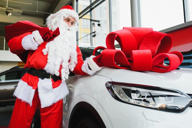 Santa Claus cerca de un coche nuevo en un concesionario de coches.