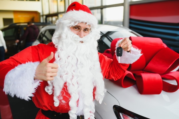 Santa Claus cerca de un coche nuevo en un concesionario de coches.