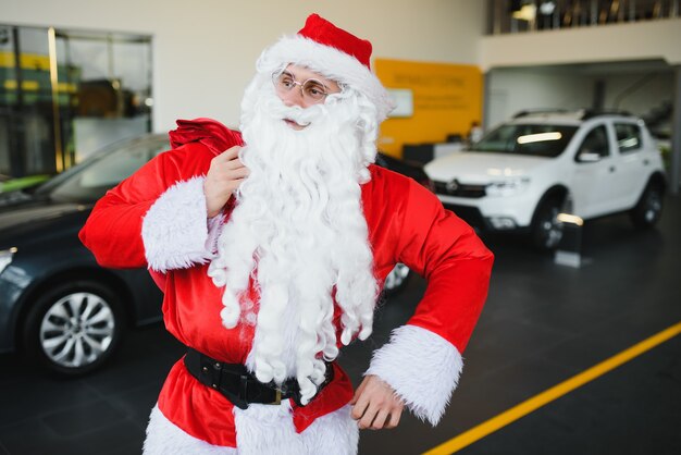 Santa Claus cerca de un coche nuevo en un concesionario de coches.