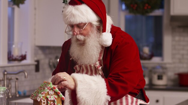 Santa Claus en la cocina decorando la casa de pan de jengibre