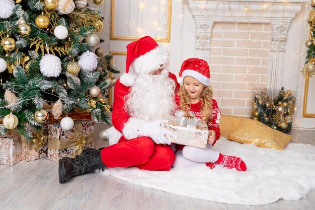 Santa Claus le da un regalo a una niña en el árbol de Navidad