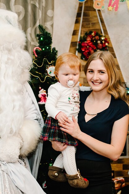 Santa Claus dando un regalo a una niña pequeña con su madre cerca de la chimenea y el árbol de Navidad en casa. Snow Maiden trajo regalos a los niños. Concepto de año nuevo. Feliz Navidad. Días festivos.