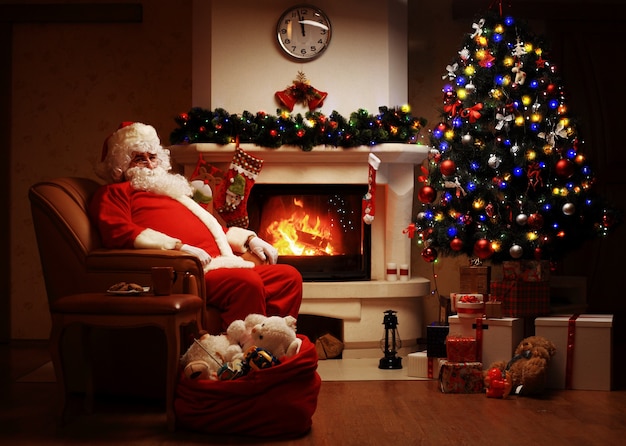 Santa Claus descansando en una silla cómoda cerca de la chimenea en casa