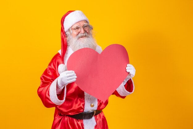 Santa Claus, die große rote Herzkarte im gelben Hintergrund hält. Romantischer Weihnachtsmann.