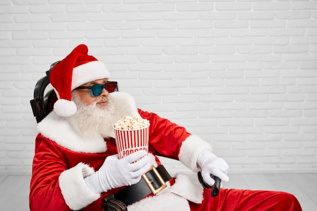 Santa Claus, die im Stuhl mit Popcorn und Fernsehzapper sitzt