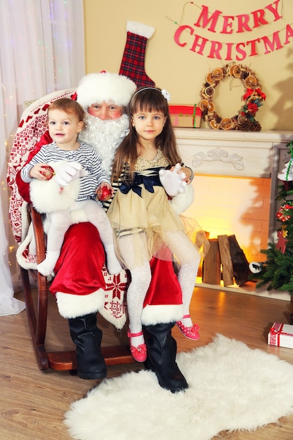 Santa Claus con dos niñas lindas junto a la chimenea y el árbol de Navidad en casa