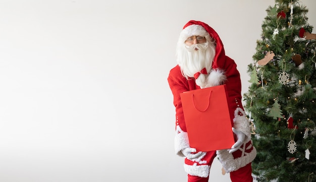 Santa Claus se encuentra cerca del árbol de Navidad con una gran bolsa de compras.