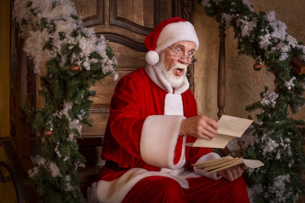 Santa Claus está leyendo las letras en el porche de la casa decorada.