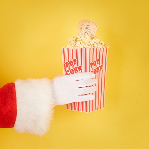 Santa Claus Hand hält einen roten und weißen Eimer mit Popcorn