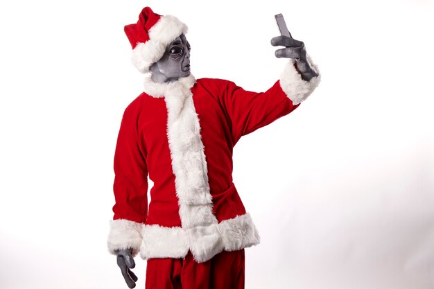 Santa Claus en máscara alienígena tomando un selfie sobre un fondo blanco.