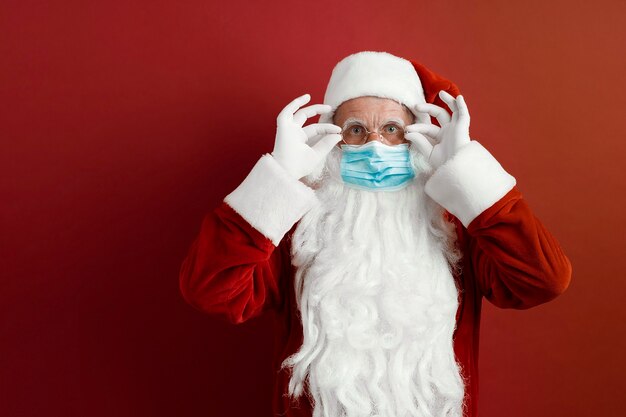 Foto santa claus en una máscara médica sobre un fondo rojo.