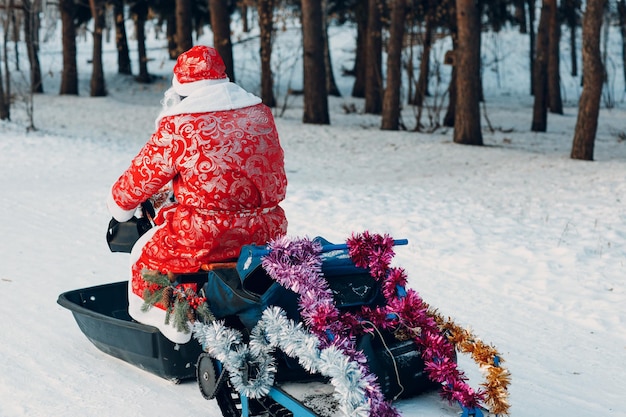 Santa claus montando motos de nieve en el bosque de invierno.