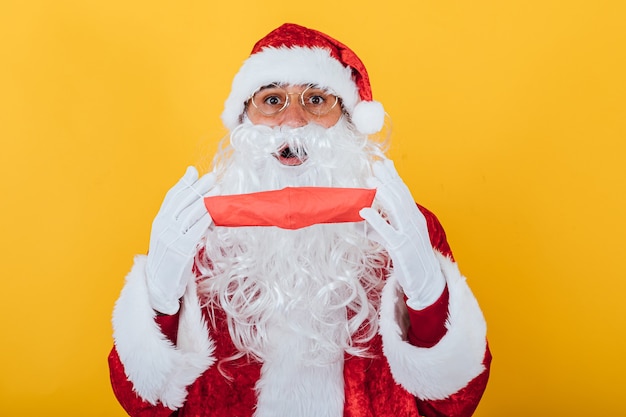 Santa Claus poniéndose una mascarilla roja, sobre amarillo