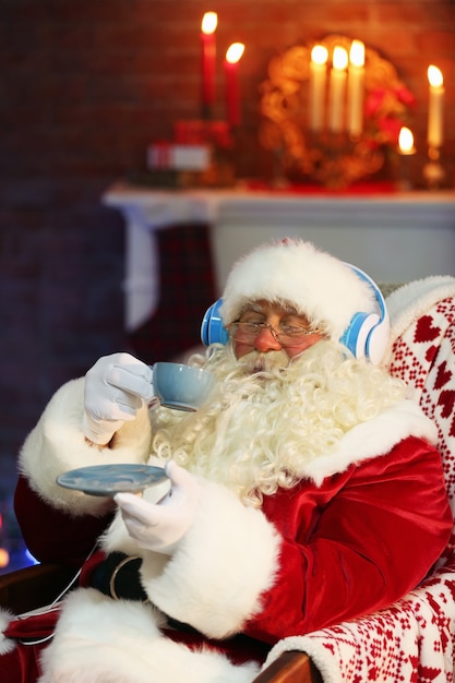 Santa Claus sentado con auriculares sentado en una cómoda mecedora en casa