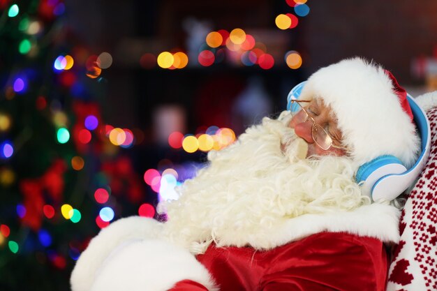 Santa Claus sentado con auriculares sentado en una cómoda mecedora en casa