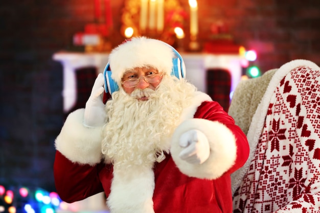 Santa Claus sentado con auriculares sentado en una cómoda mecedora en casa