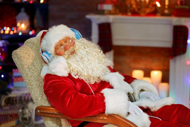 Santa Claus sentado con auriculares sentado en una cómoda mecedora en casa