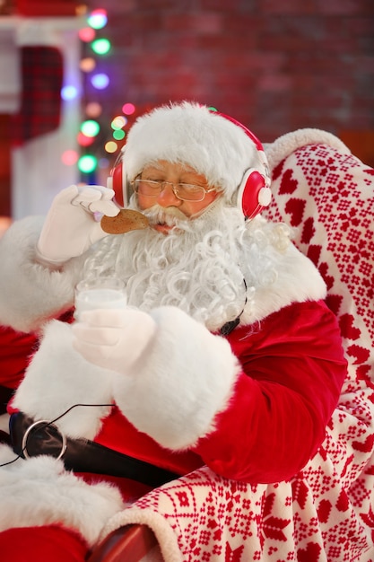 Santa Claus sentado con auriculares sentado en una cómoda mecedora en casa