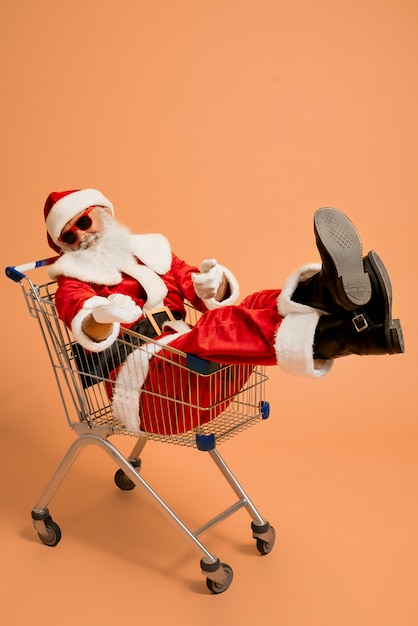 Santa Claus sentado en el carrito de compras y mostrando signo super