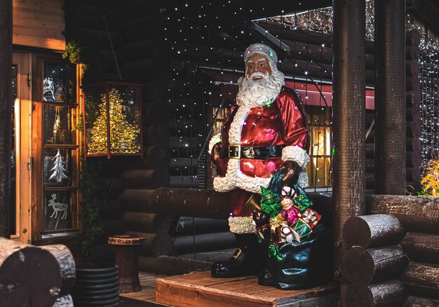 Santa Claus sentado en el porche de una casa de madera con adornos navideños