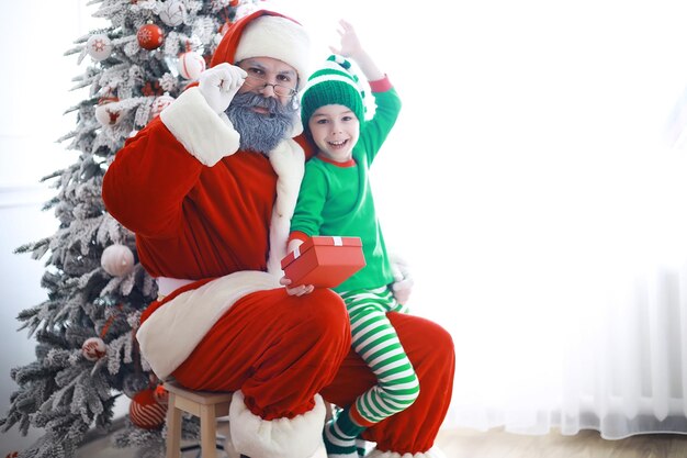 Santa Claus sitzt mit kleinen niedlichen Elfen über Weihnachten Hintergrund Zeit der Wunder Geschenke vom Weihnachtsmann