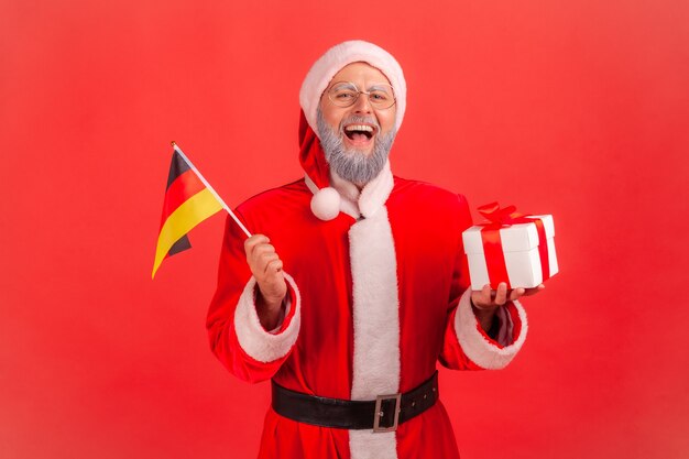 Santa claus sosteniendo la bandera alemana y caja con regalo de Navidad.