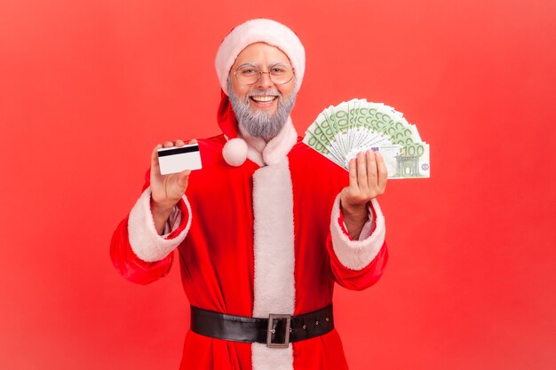 Santa claus sosteniendo mostrando el ventilador de los billetes en euros y la tarjeta de crédito en las manos.