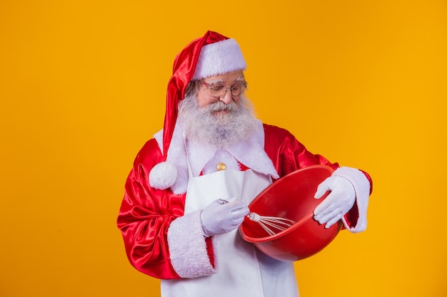 Santa Claus con un tazón batiendo la torta sobre fondo amarillo