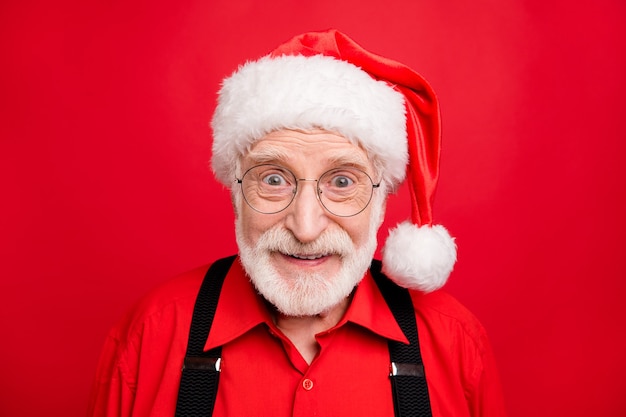 Santa Claus en tirantes y sombrero posando en la pared roja