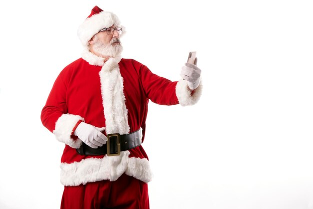 Santa Claus tomando un selfie con un teléfono móvil sobre un fondo blanco.