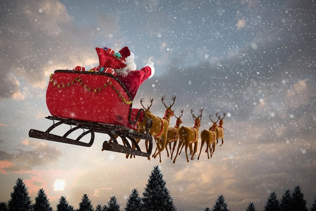 Santa Claus en trineo con caja de regalo contra la nieve que cae sobre el bosque de abetos