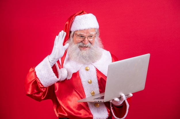 Santa Claus usando una computadora portátil sobre fondo rojo.