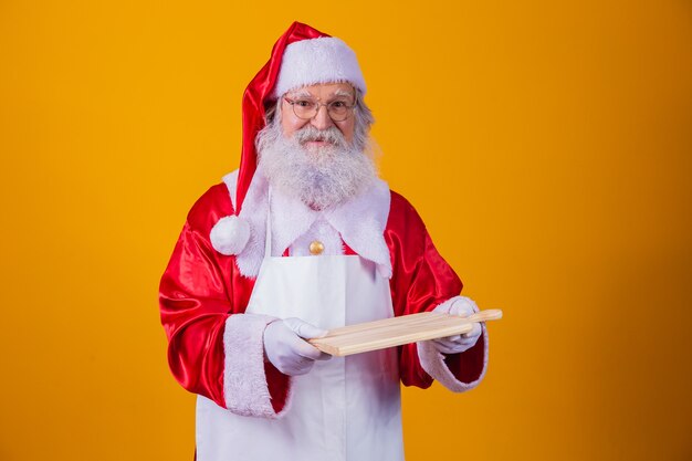 Santa Claus vestido con delantal con tablero de carne vacío sobre fondo amarillo.