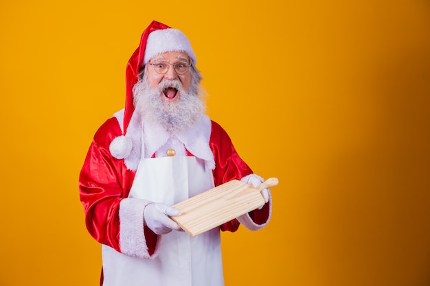 Santa Claus vestido con delantal con tablero de carne vacío sobre fondo amarillo.