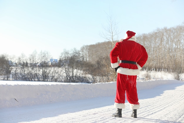 Santa Claus viene con regalos del exterior. Santa con traje rojo con barba y gafas está caminando por el camino hacia la Navidad. Papá Noel trae regalos a los niños.