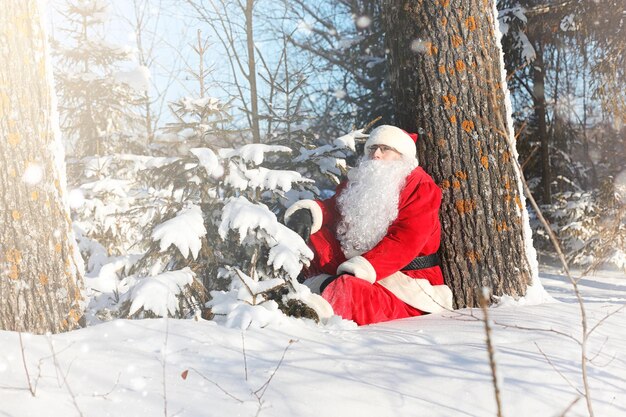 Santa Claus viene con regalos del exterior. Santa con un traje rojo con barba y gafas está caminando por el camino hacia la Navidad. Papá Noel trae regalos a los niños.