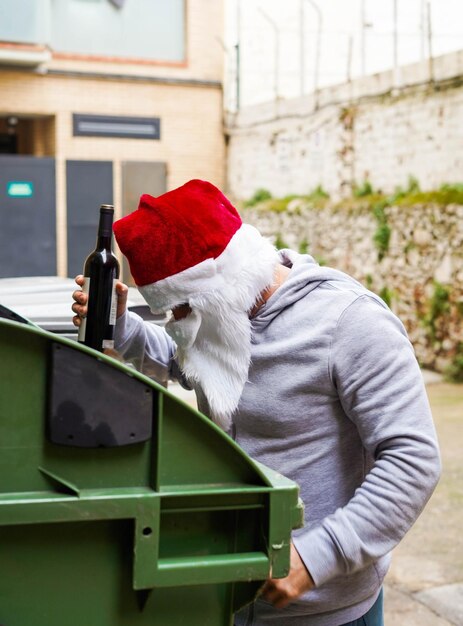 Santa sin hogar bebiendo vino y hurgando en los contenedores de basura.