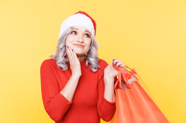 Santa Mädchen in der Mütze, die große Taschen mit Geschenken lokalisiert im gelben Studio hält