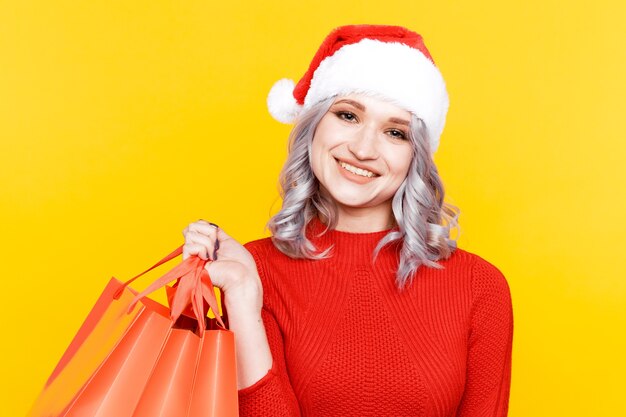 Santa niña en el sombrero sosteniendo grandes bolsas con regalos aislados en la pared amarilla