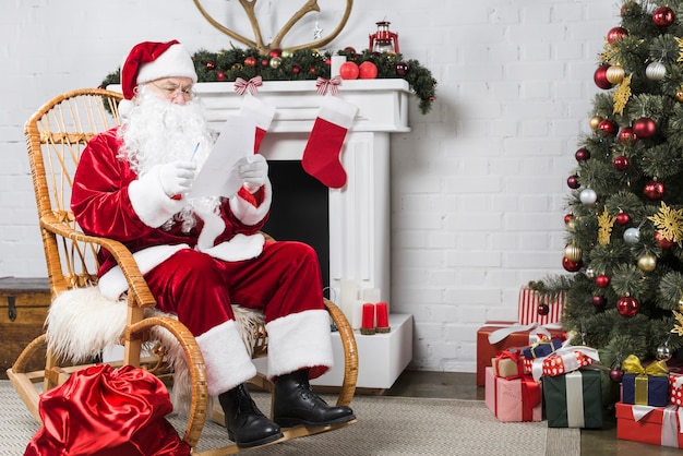 Foto santa sentado en la mecedora cerca de árbol de navidad